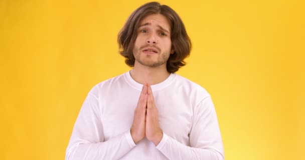 Jongeman bedelend voor iets, hand in hand in gebed gebaar en pleiten voor camera, oranje studio achtergrond — Stockvideo