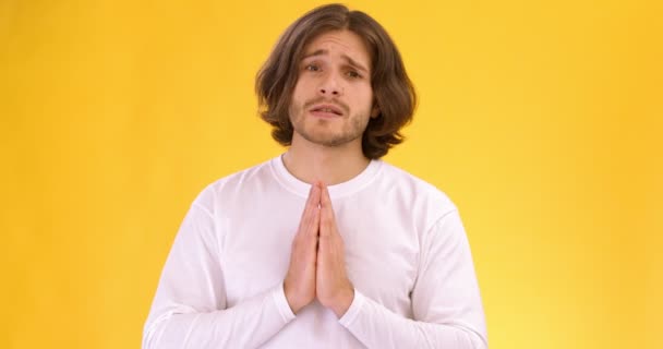 Joven mendigando por algo, tomándose de la mano en gesto de oración y suplicando a la cámara, fondo naranja estudio — Vídeos de Stock