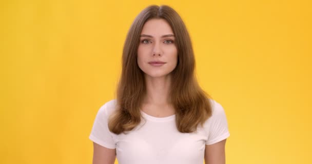 Studio πορτρέτο της όμορφης ήρεμης κυρίας σε λευκό t-shirt κοιτάζοντας κάμερα, κίτρινο φόντο — Αρχείο Βίντεο
