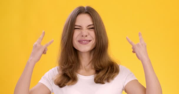 Студийный кадр молодой веселой женщины, показывающей жест панк-рога, оранжевый фон, замедленная съемка — стоковое видео