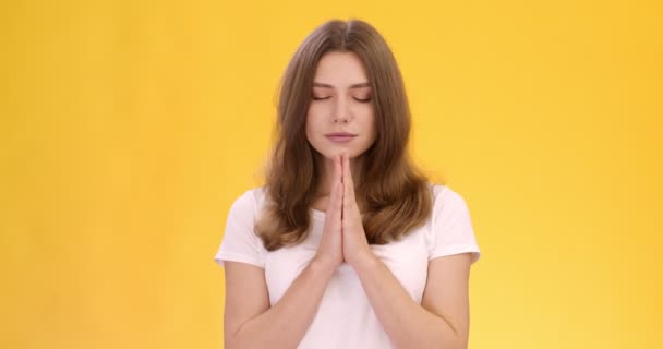 Молодая мирная женщина молится Богу, сжимая руки и закрывая глаза во время медитации, оранжевый студийный фон — стоковое видео