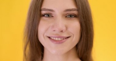 Kameraya gülümseyen mutlu genç bayanın portresini yakından çek, turuncu stüdyo arka planı, yavaş çekim.