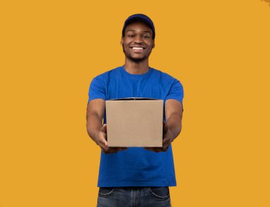 Siyah teslimatçı elinde karton kutuyla kameraya gösteriyor.