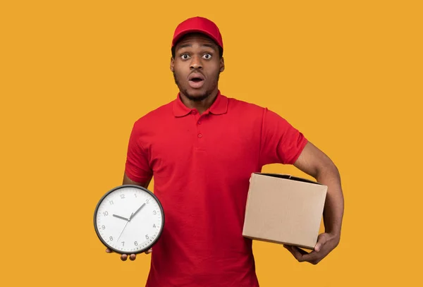 Sorprendido repartidor negro hombre caja de espera y reloj — Foto de Stock