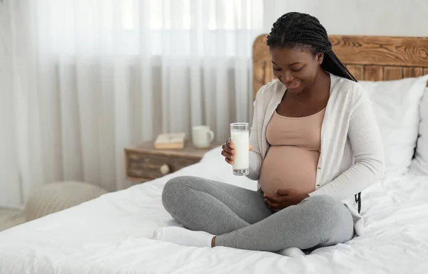 Sonriente mujer embarazada negra bebiendo un vaso de leche fresca en casa — Foto de Stock