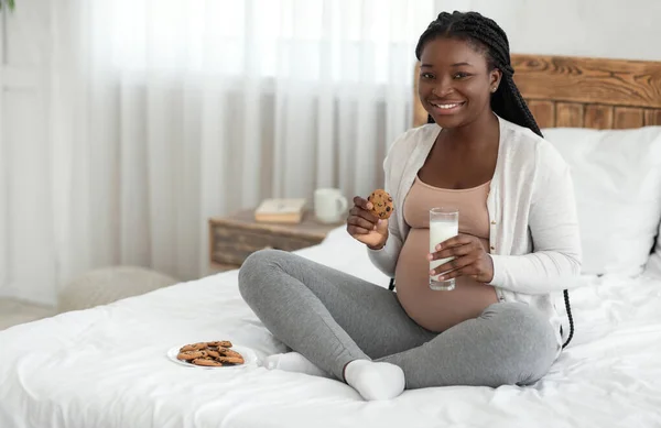 Czas na przekąskę. Szczęśliwa Czarna Pani w ciąży o gryzie ciasteczka i mleko — Zdjęcie stockowe