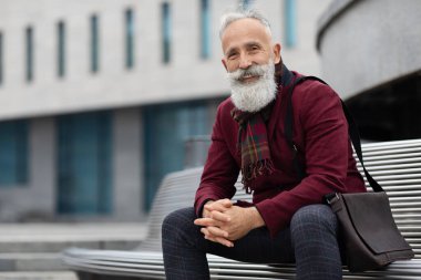 Yakışıklı son sınıf öğrencisi bankta oturuyor, kameraya gülümsüyor.