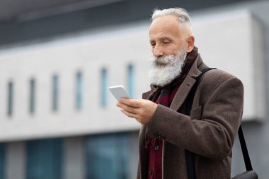 Yaşlı gri saçlı işadamı sokakta akıllı telefon kullanıyor.