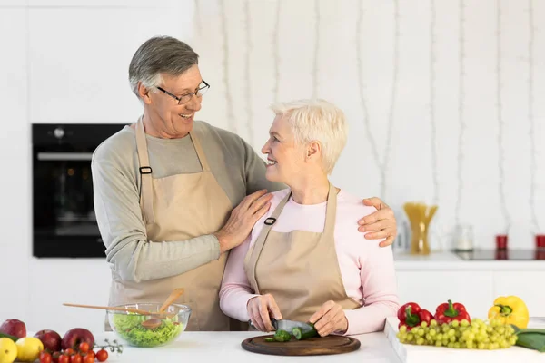 Felices cónyuges mayores cocinando haciendo ensalada de pie en la cocina al aire libre —  Fotos de Stock