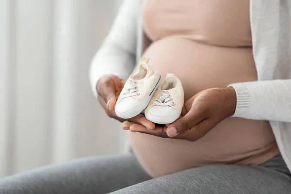 Nascita in attesa. nero incinta madre seduta con poco bambino scarpe in mani — Foto Stock