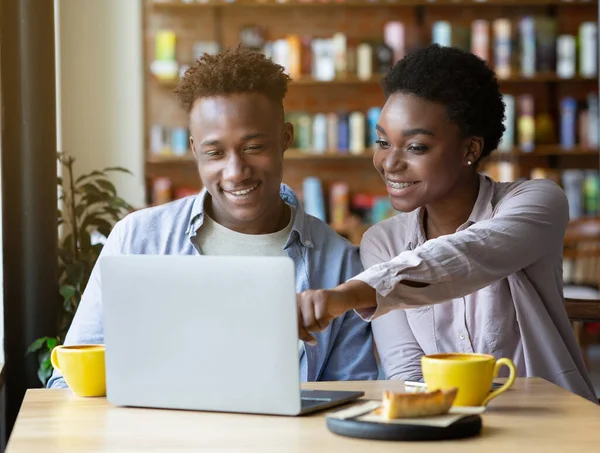 Mulher negra bonita apontando para a tela do laptop, mostrando algo para seu namorado no café — Fotografia de Stock