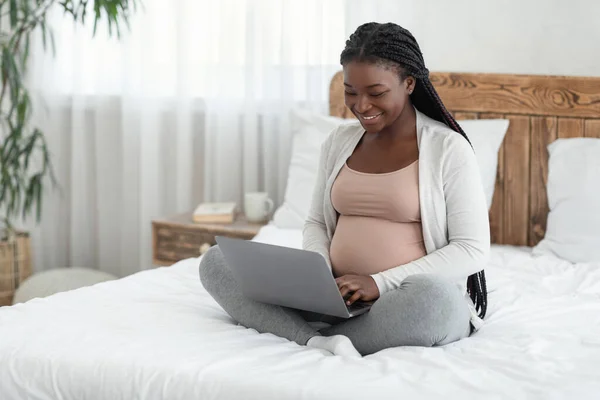 Online winkelen. Vrolijke zwarte verwachte moeder met behulp van laptop computer thuis — Stockfoto