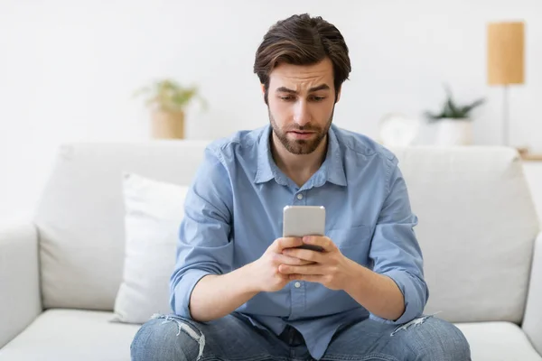 Frustrated Man Using Cellphone Texting Sitting On Sofa At Home — Stock Photo, Image