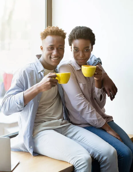 Couple noir positif assis sur le rebord de la fenêtre et boire du café aromatique au café — Photo