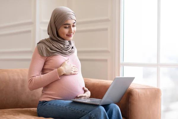 Těhotná muslimská žena pomocí notebooku prohlížení internetu sedí doma — Stock fotografie