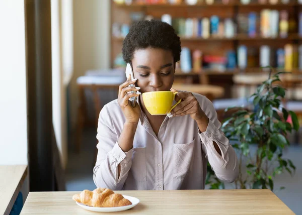 Bastante señora negra hablando por teléfono celular mientras bebe café en el acogedor café — Foto de Stock