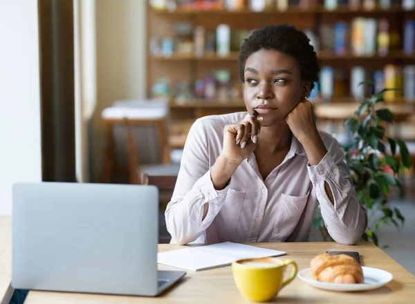 Fiatal fekete nő notebook közelében ül laptop kávézóban, mélyen a gondolat, tanul vagy dolgozik online, másolás tér — Stock Fotó