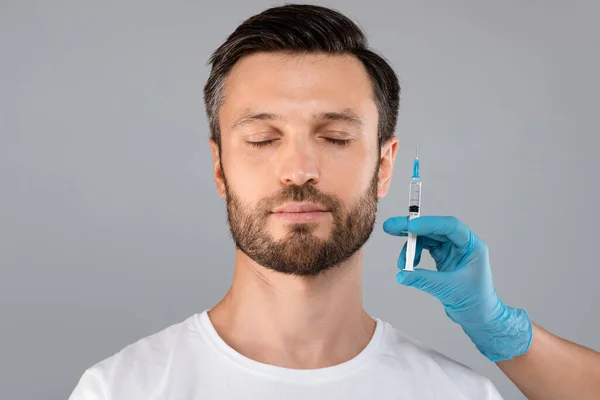 Бородатий чоловік із закритими очима та лікарська рука з шприцом — стокове фото