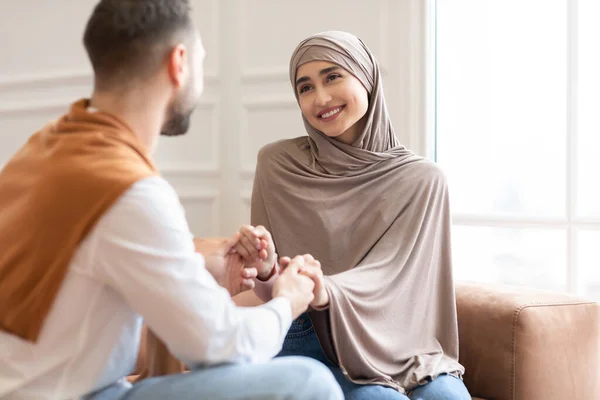 Любящие мусульмане держатся за руки, сидя дома на диване — стоковое фото