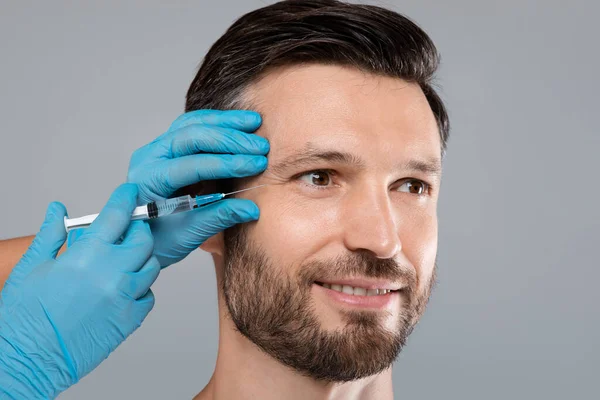 Closeup of happy handsome bearded man getting under eye injection — Stock Photo, Image