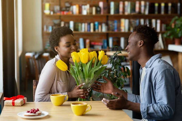 ハンサムな黒男与えます彼のガールフレンド花束のチューリップとギフトのためにValentines Dayでcaf é — ストック写真