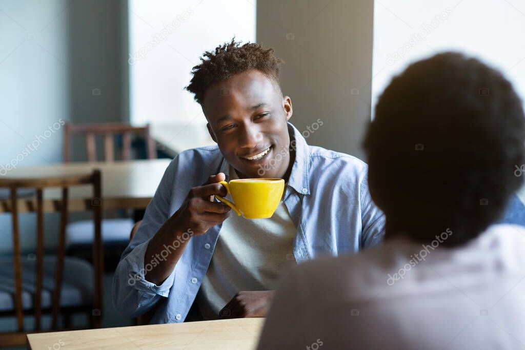 Adorable black couple chatting in coffee shop at lunchtime, having first date, starting romantic relationship