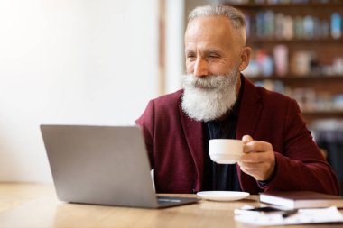 Kahve içip dizüstü bilgisayar kullanan üst düzey bir adam.