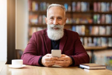 Kafede cep telefonu kullanan neşeli, yaşlı, gri saçlı adam.