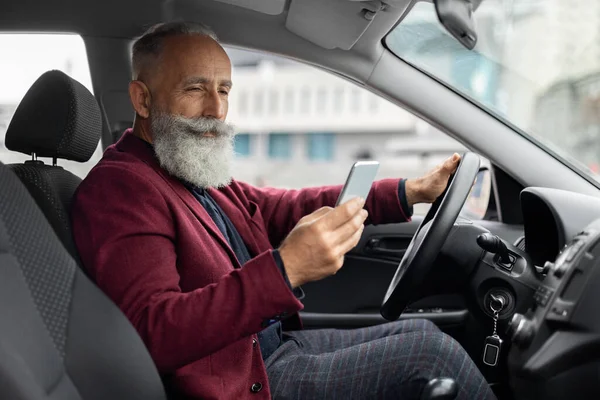 Homme âgé conduisant une nouvelle voiture, en utilisant un téléphone mobile — Photo