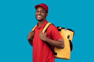 Siyah teslimatçı termal çantayla kameraya bakıyor.