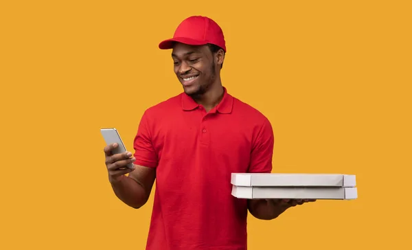 Černý doručovatel drží krabice od pizzy, pomocí smartphonu — Stock fotografie