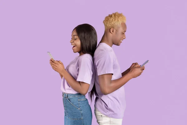 Seitenansicht eines jungen afroamerikanischen Paares mit Mobiltelefonen über violettem Studiohintergrund — Stockfoto