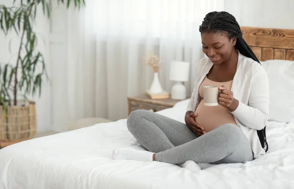 Sonriente negro embarazada madre relajante en casa con taza de té de hierbas — Foto de Stock