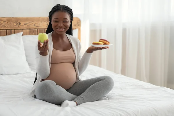 Dieta del Embarazo. Mujer embarazada sonriente eligiendo manzana verde en lugar de rosquillas malsanas — Foto de Stock