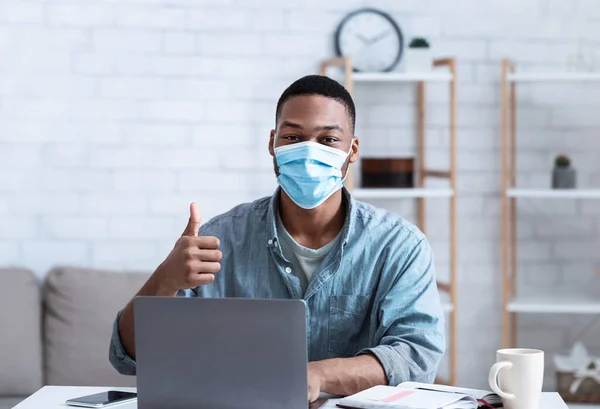 Homem africano vestindo máscara sentado no laptop Gesturing Thumbs-Up interior — Fotografia de Stock