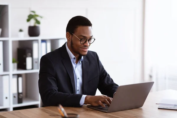 Vrolijke zwarte ondernemer werken met laptop, kantoor interieur — Stockfoto