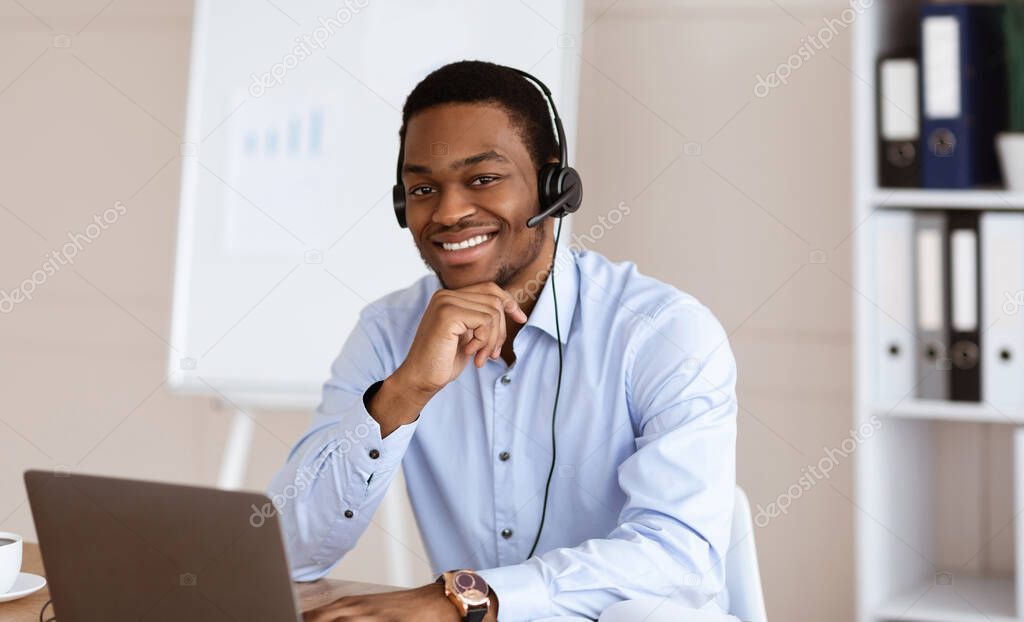 Cheerful black man with headset using laptop in office