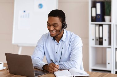 Neşeli siyahi adam kriz yöneticisi dizüstü bilgisayarın önünde çalışıyor.