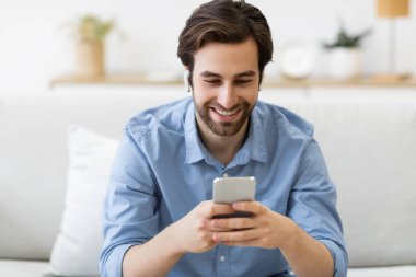 Oturma odasında akıllı telefondan cep telefonu oyunu oynayan adam.