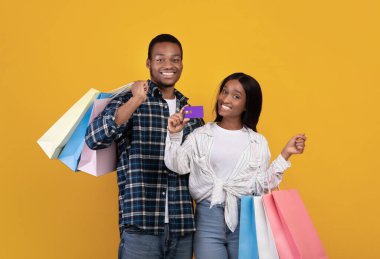 Gülümseyen Afrikalı genç Amerikalı öğrenciler bir sürü renkli alışveriş torbası olan çiftler kredi kartı gösteriyor.