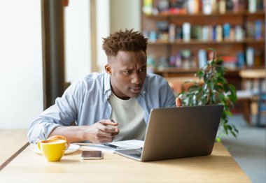 Zor sınavlar için internetten ders çalışan sinirli siyahi bir adam, Kafe 'de sıkı bir iş projesi üzerinde çalışmak için dizüstü bilgisayar kullanıyor.