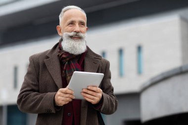 Dijital tabletli neşeli yaşlı adam sokakta yürüyor.