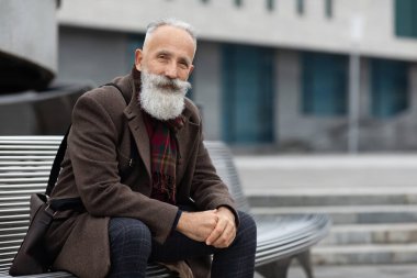 Yakışıklı son sınıf öğrencisi sokakta bankta oturuyor.