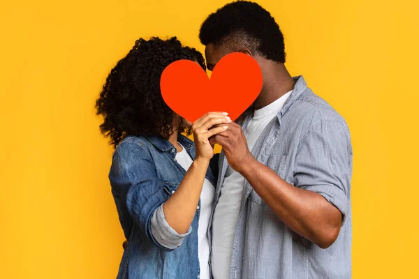 Tajná láska. Romantický černošky pár skrývá a líbání za červeným papírem srdce — Stock fotografie
