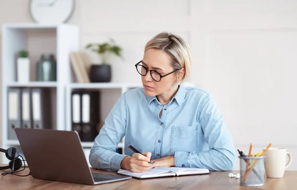 Mujer centrada en escribir información durante la formación empresarial o reunión en línea, participando en la conferencia web desde casa — Foto de Stock