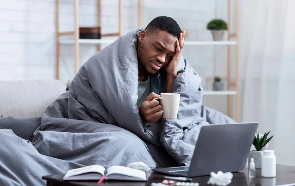 Hombre africano enfermo usando portátil teniendo fiebre y dolor de cabeza en el interior — Foto de Stock