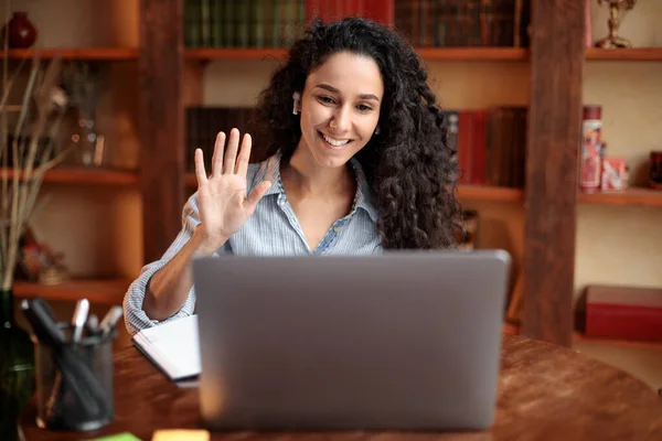 Mulher sentada na mesa, usando computador e acenando para webcam — Fotografia de Stock