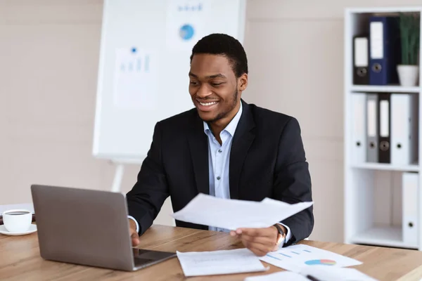 Щасливий чорний бізнесмен перевіряє звіти в сучасному офісі — стокове фото