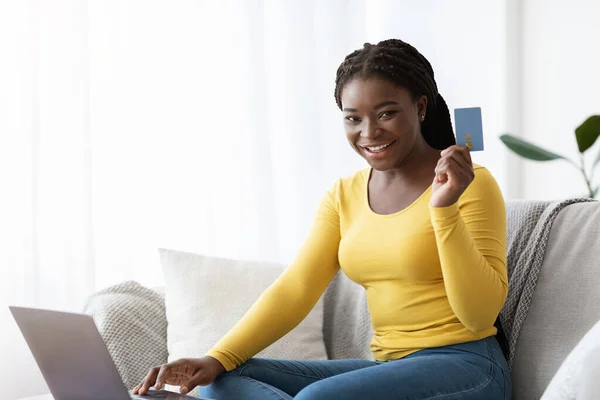 Shopping online. Felice signora africana con carta di credito e computer portatile a casa — Foto Stock