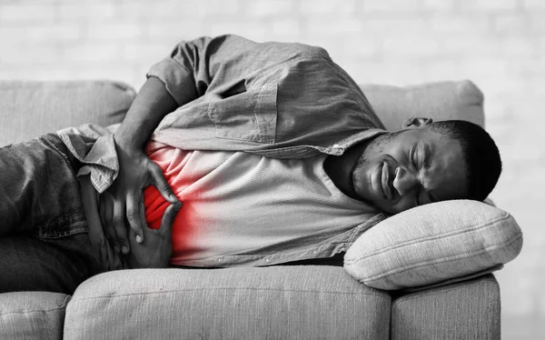 Африканський чоловік, що має стомач, лежить на дивані вдома, чорно-білий — стокове фото
